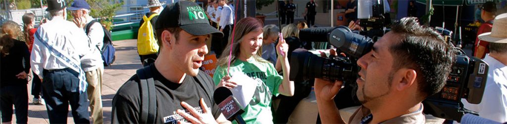 an image of a man being interviewed at an outdoor rally with many other protestors and supports behind him