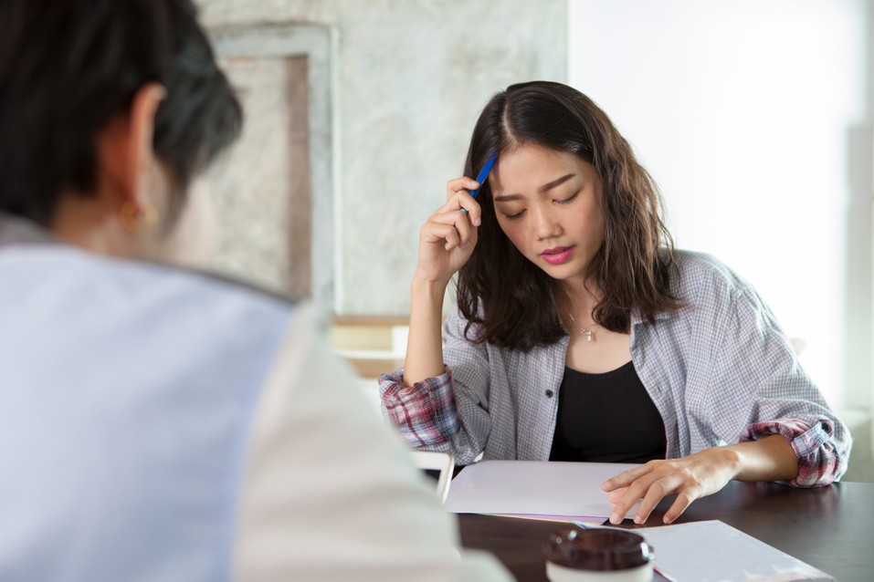 Woman reviewing paperwork at a table while speaking with another person.